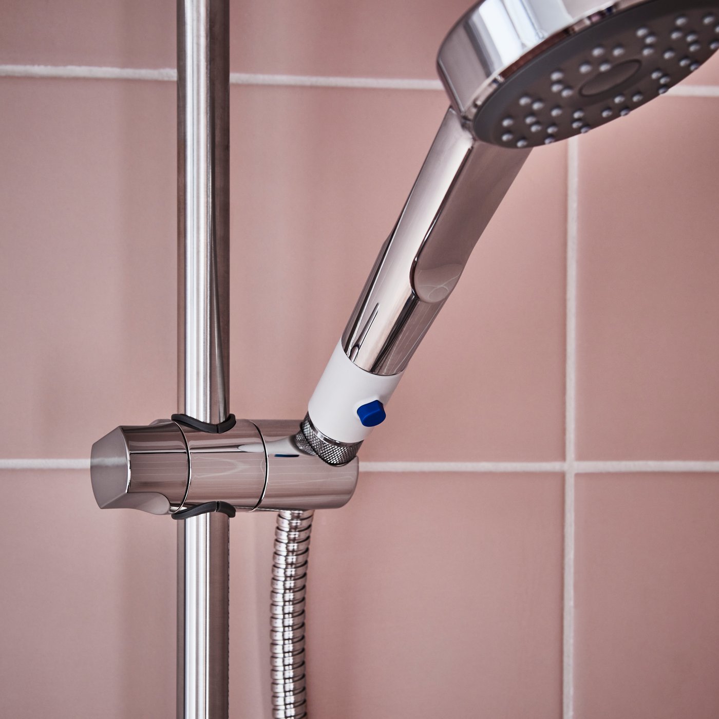 A close-up of a chrome-plated BROGRUND riser rail with handshower kit in a shower with peachy tiles.
