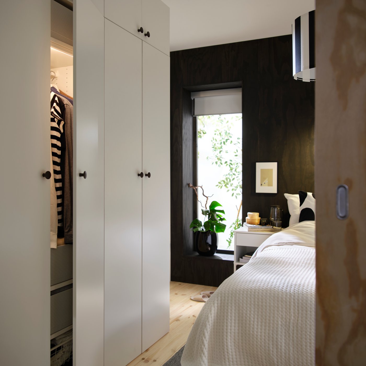 LASTARE wardrobe combination in white with partially open door showing hanging clothes beside a bed in a modern bedroom.