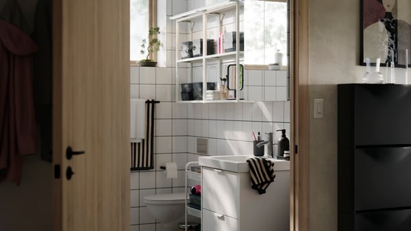 A bright and modern bathroom with white HAVBÄCK/ÖRRESJÖN storage, white open ENHET shelves on the wall and striped towels.