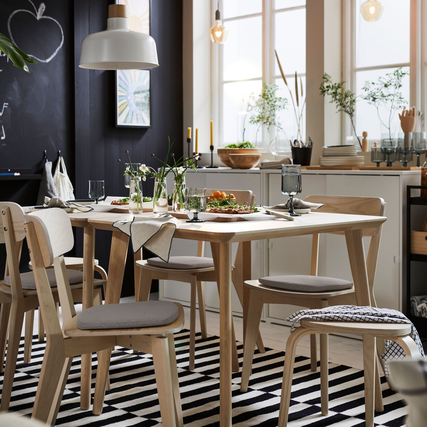 Two LISABO tables in ash veneer and several LISABO chairs in ash are standing on a STOCKHOLM rug in black and off-white.