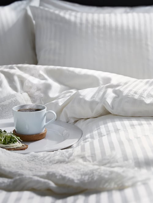 A pillow and quilt covered in NATTJASMIN bedlinen. The quilt is folded back at one corner.