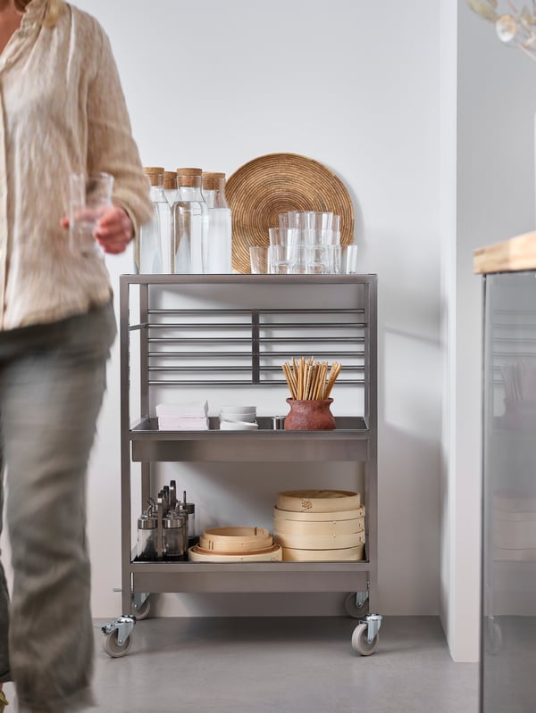 A metal kitchen island on wheels stocked with jarred ingredients sits next to a kitchen counter.
