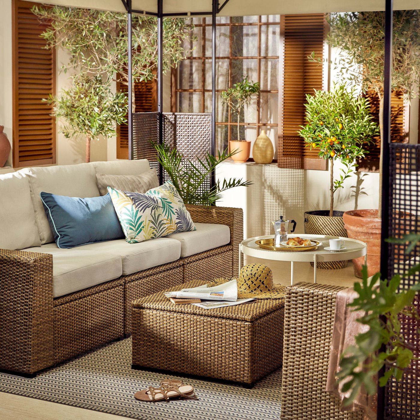 Mesa de centro de mimbre con almacenaje en frente de un sillón de mimbre con cojines blancos y azules.