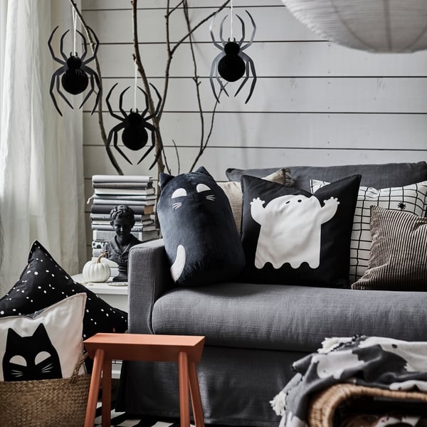 Wohnzimmer mit Halloween-Deko wie Spinnen an der Wand und Kissen mit Katzen- und Geistermotiven