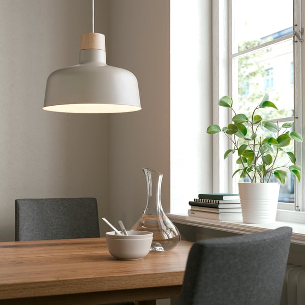 Una habitación con una mesa de madera y dos sillas grises, una en frente de la otra. Sobre la mesa una lámpara colgante BUNKEFLO.