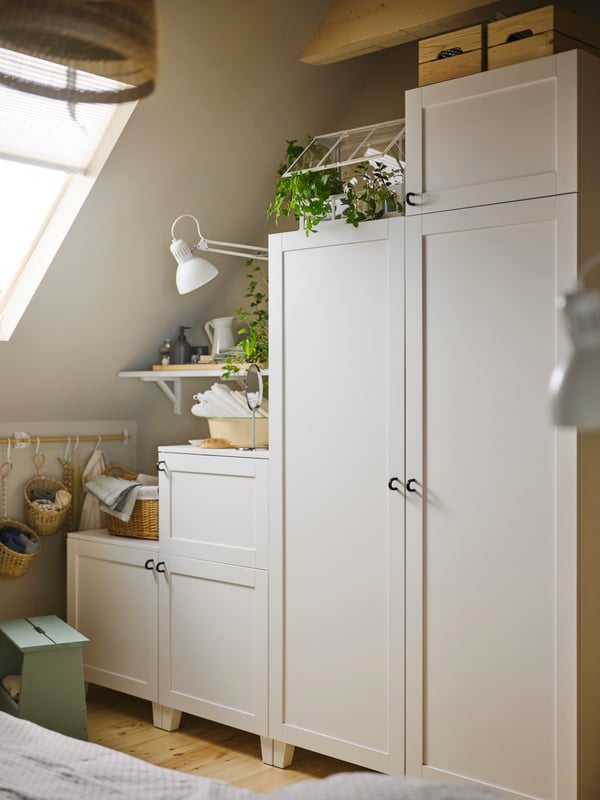 Ein weisser PLATSA-Kleiderschrank mit 6 Türen auf verschiedenen Ebenen in der Ecke eines Raumes mit schräger Decke.