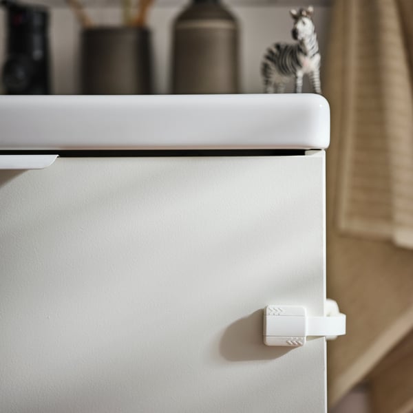 A toy zebra on an ENHET bathroom cabinet with an UNDVIKA multi latch on the side and various bathroom articles behind.