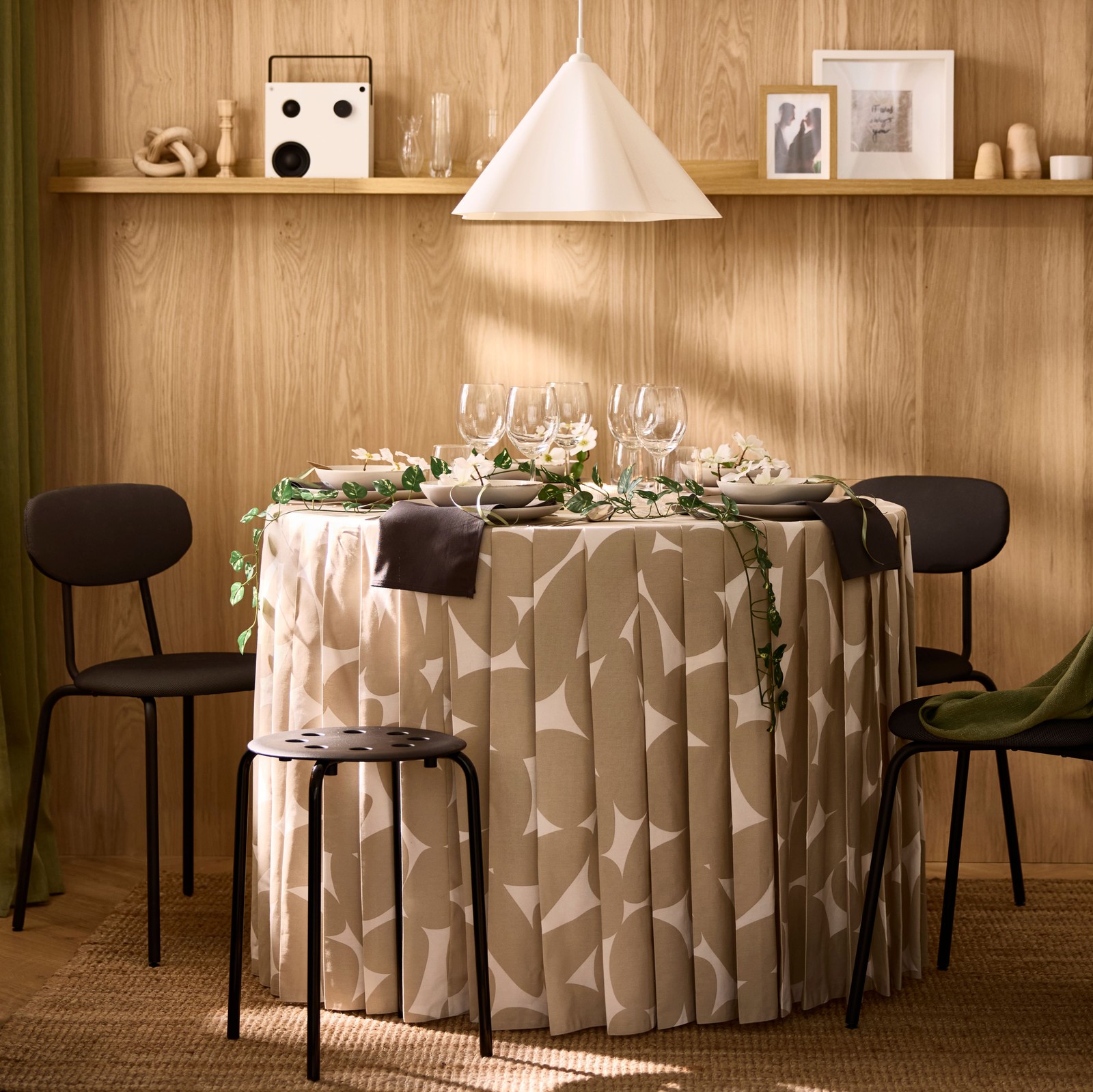 Unha mesa de comedor redonda decorada para unha ocasión especial, cun mantel plisado que chega ao chan e que está feito con tea VITFRYLE.