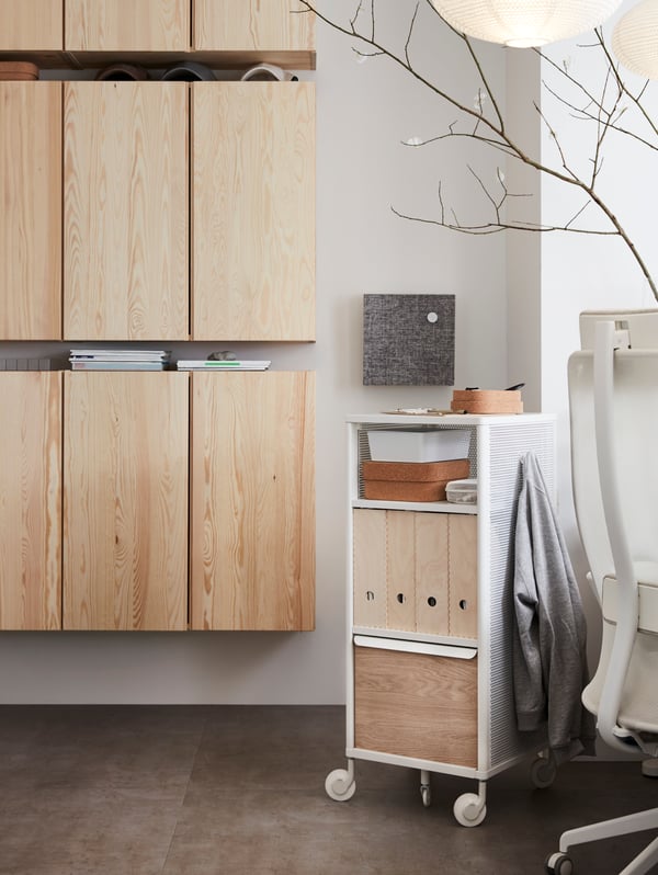 IVAR pine wall cabinets, a white mesh storage unit on castors and the edge of a swivel chair, in an office space.