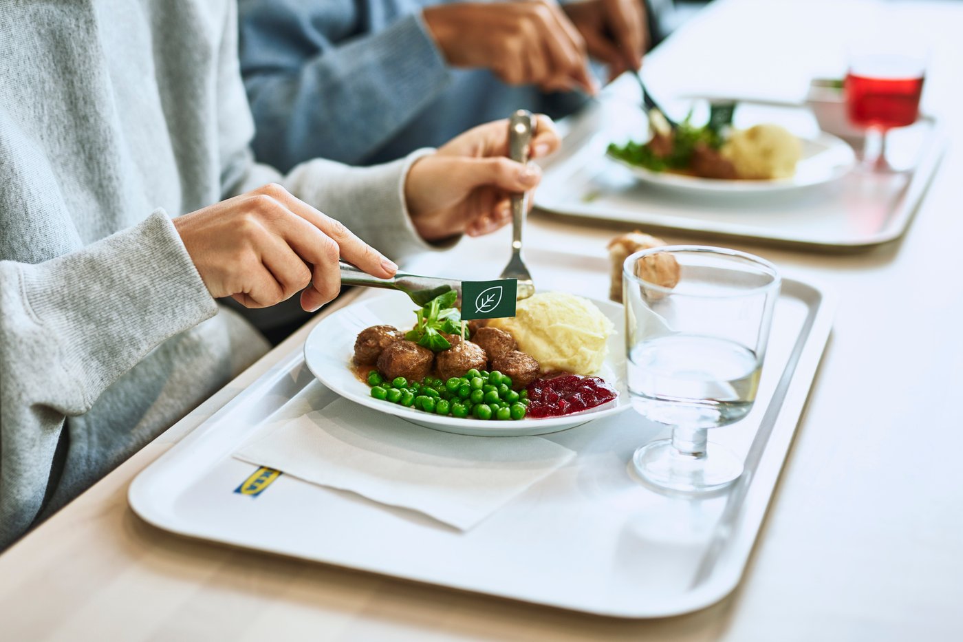 Lähikuvassa kaksi ihmistä ruokapöydän ääressä vierekkäin syömässä pyörykkäannoksia, jotka ovat IKEA-tarjottimella.