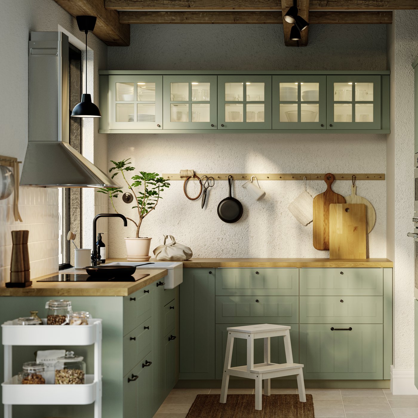 Ett kök med ljusgröna STENSUND fronter, en svart GRUNDAD induktionshäll och en väggmonterad MATTRADITION köksfläkt.