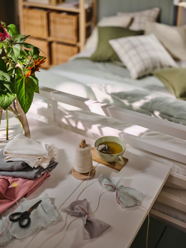 A white HAUGA drop leaf extendable table at the end of a TARVA bed with anthracite white check EKTANDVINGE bed linen on it.