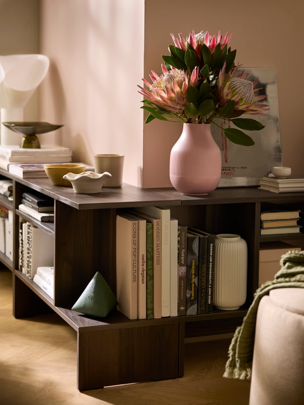 HOLMERUD side tables filled with books and decoration follow the outline of an outward corner in a sunlit room.