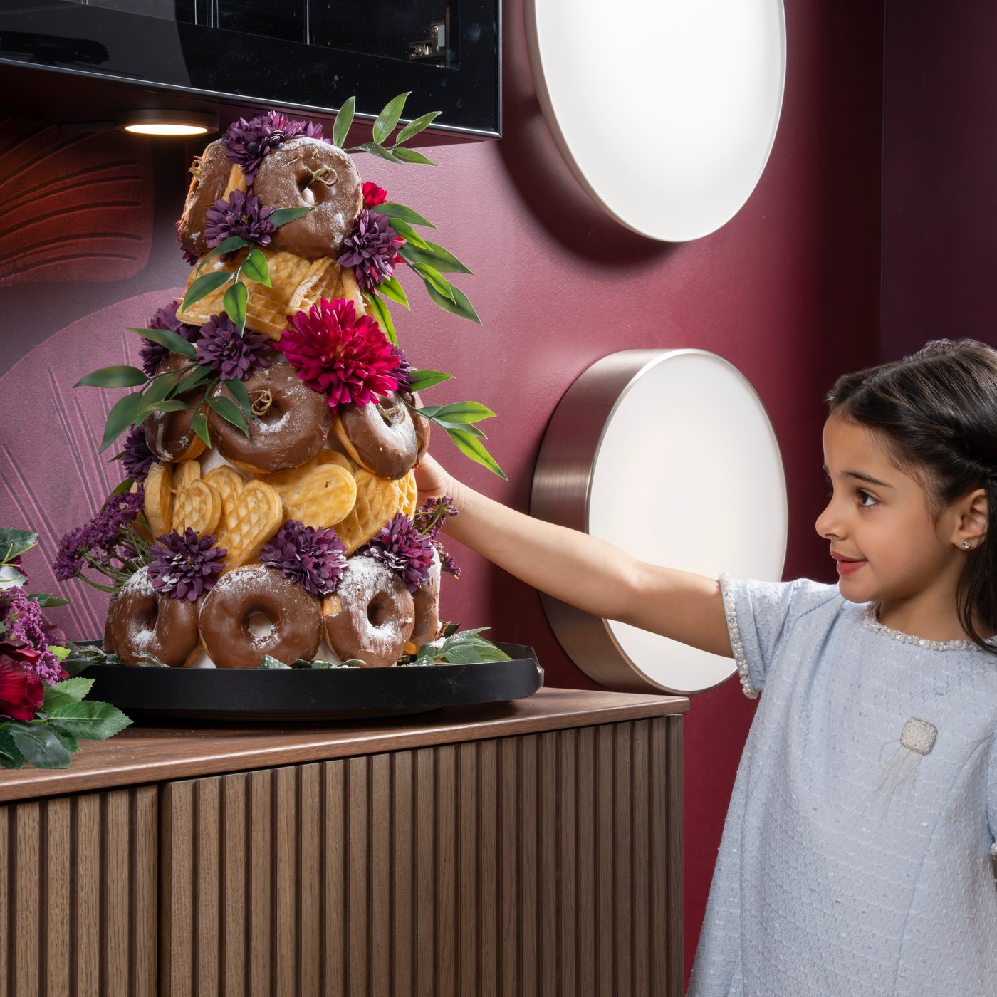 Child reaching for a doughnut from a doughnut tower.