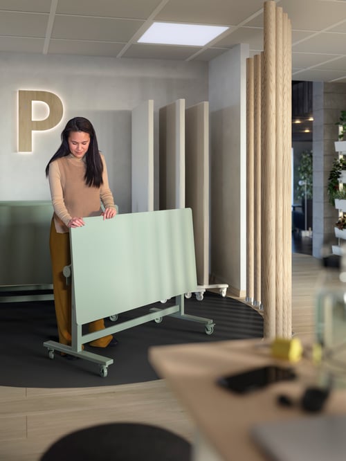 A person is moving a green MITTZON foldable table with castors, and behind them there are three frames with castors.