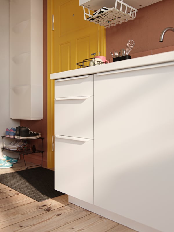 Kitchen cabinets with VALLSTENA fronts in white against a terracotta-colored wall, tiles, and yellow front door.