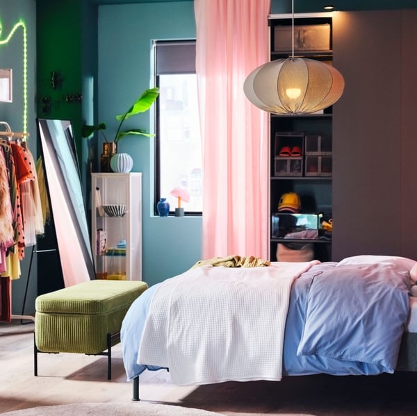 A turquoise, oval, REGNSKUR pendant lampshade hangs above a TÄLLÅSEN upholstered bed with blue-grey ÄNGSLILJA bedding.