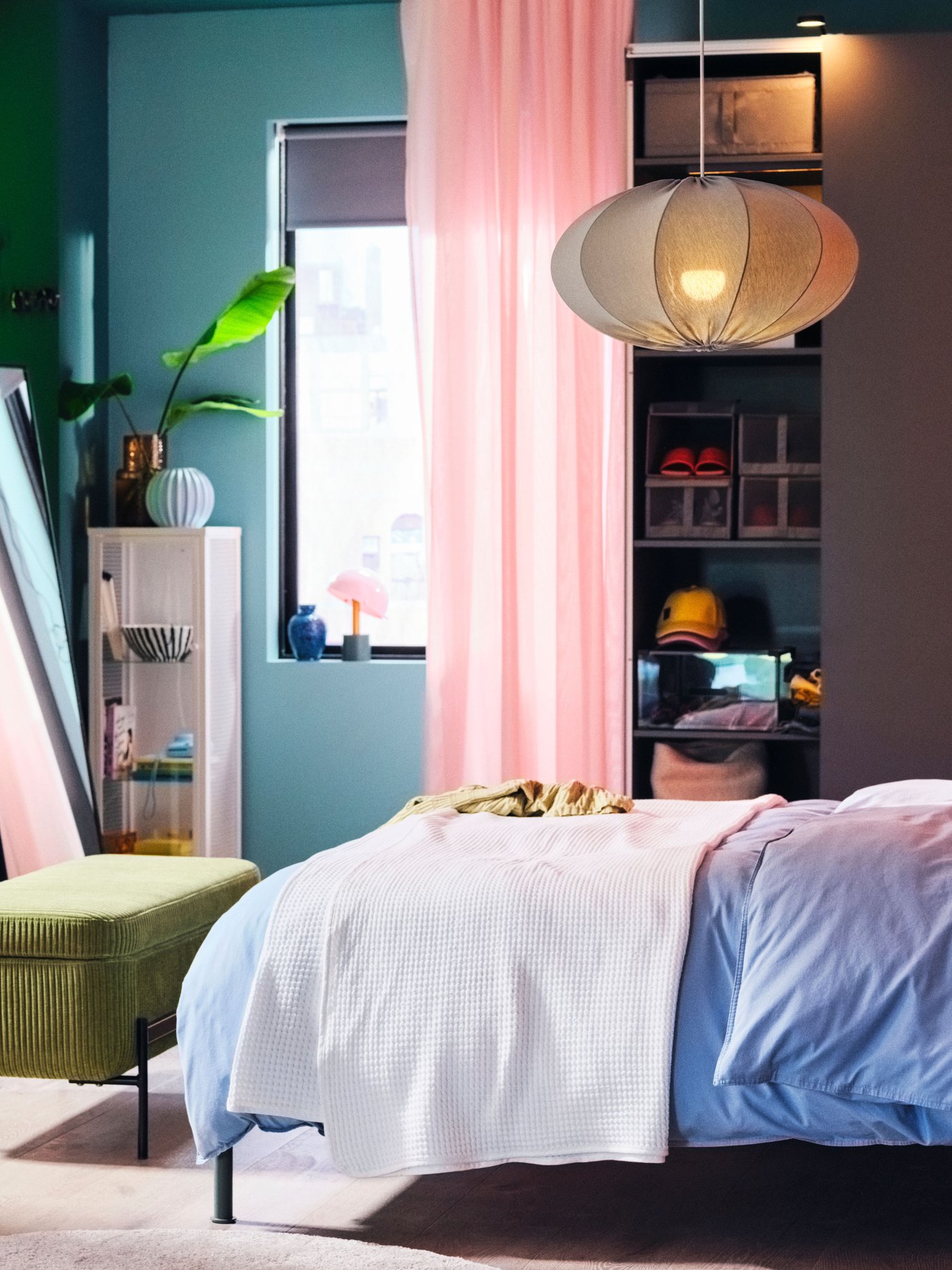 A turquoise, oval, REGNSKUR pendant lampshade hangs above a TÄLLÅSEN upholstered bed with blue-grey ÄNGSLILJA bedding.