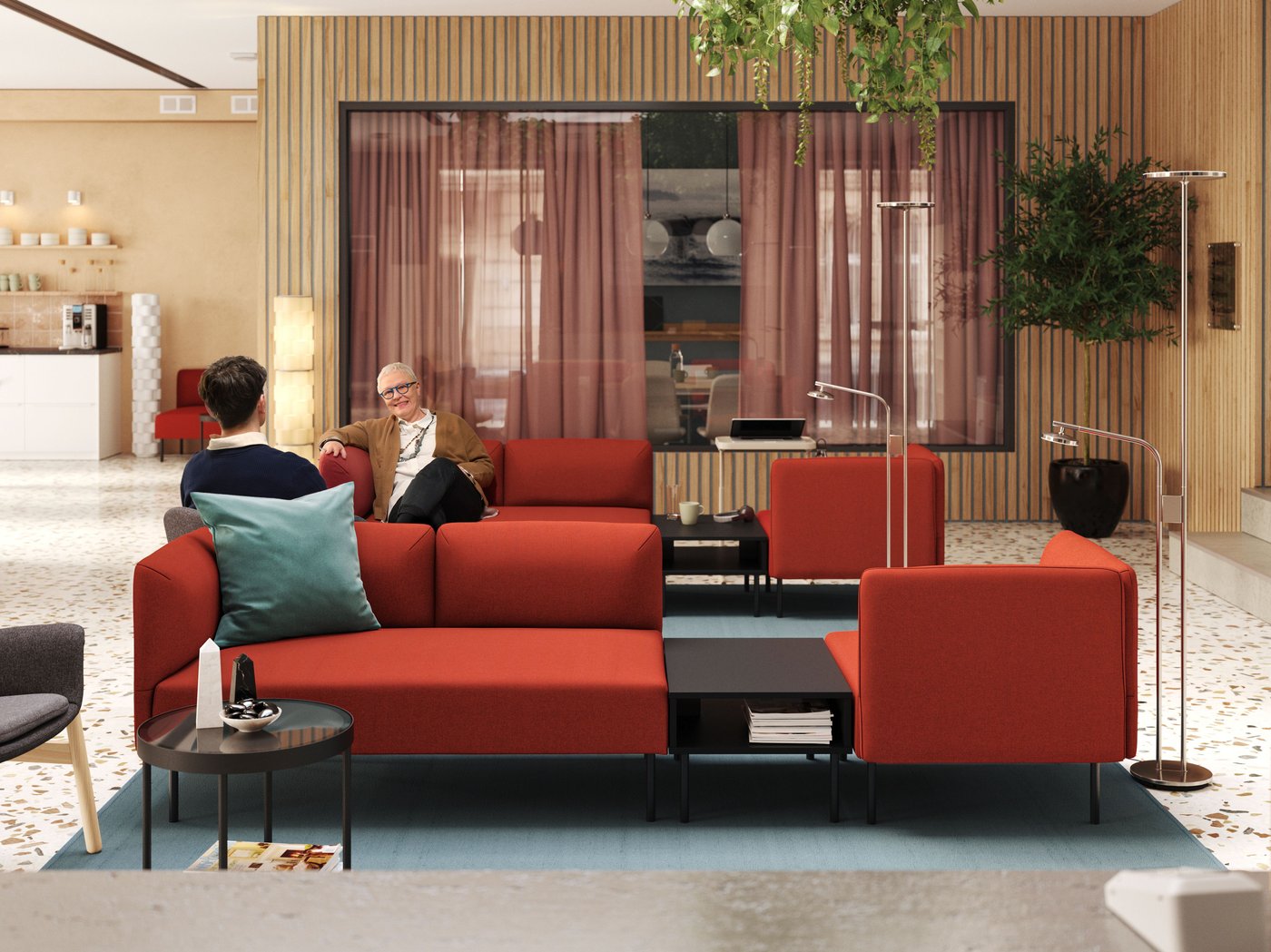 Dues persones es relaxen en un vestíbul molt lluminós d'estil modern que funciona també com a sala de reunions, al centre del qual hi ha dos sofàs modulars LILLEHEM de color vermell.