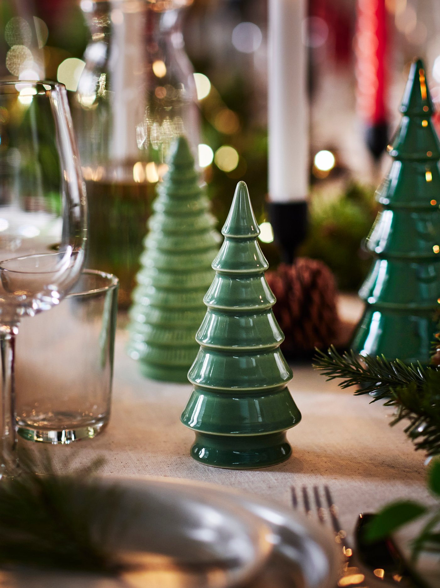 Three green VINTERFINT Christmas decorations on a festve dining table beside drinking glasses.