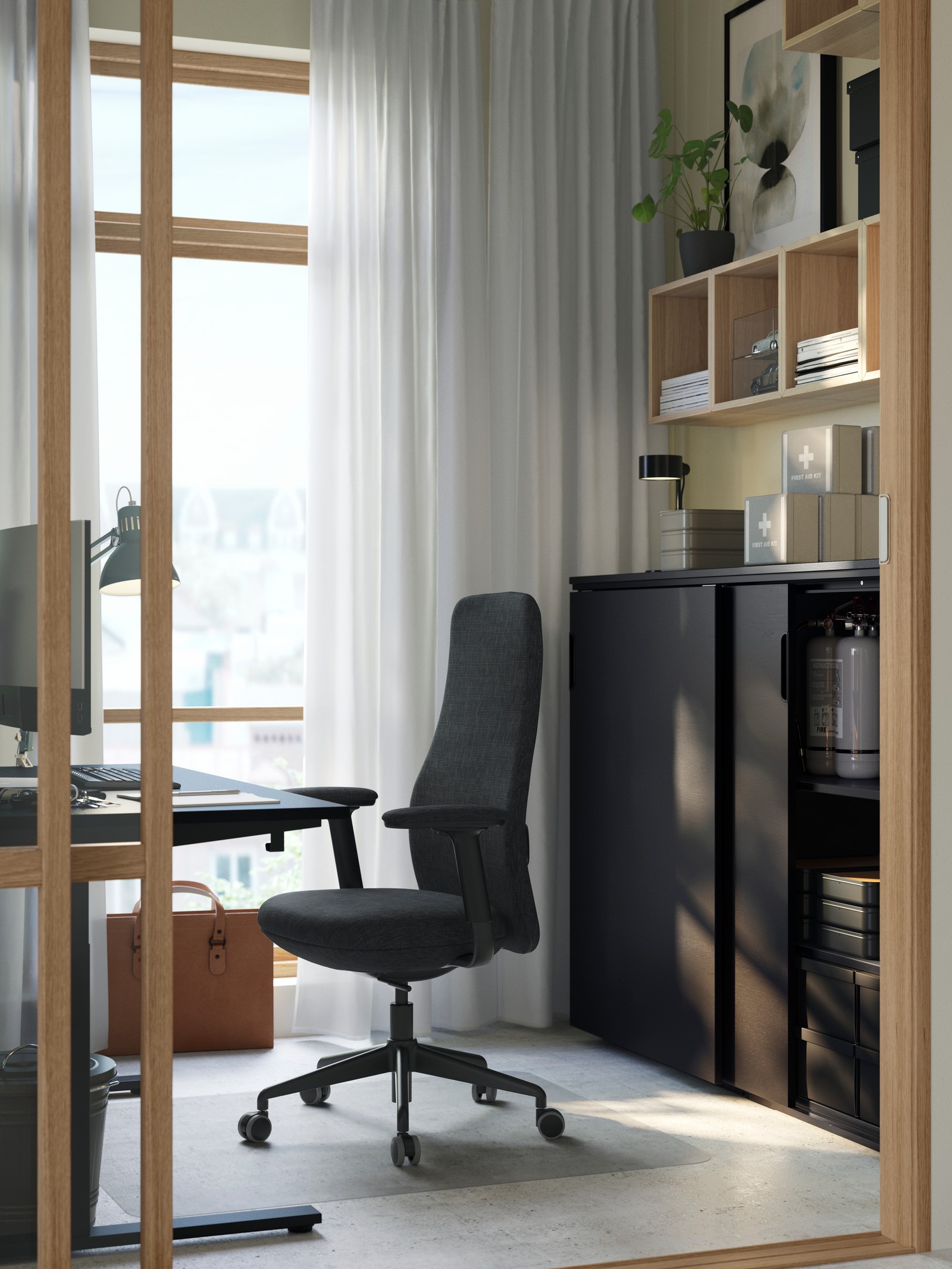 A small light-filled room with a workstation of a black GRÖNFJÄLL chair and a black GALANT cabinet with sliding doors.