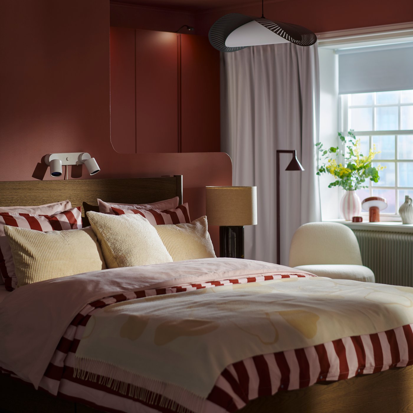 A bedroom with dark brown TONSTAD bed made with striped SLÅNHÖSTMAL bedding and cream pillows and throw with a window behind.