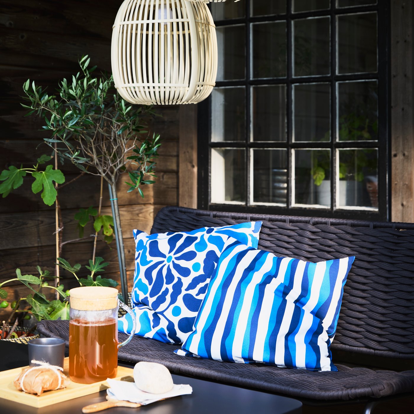 TEGELÖN black sofa with blue and white pillows, a table set with a 365+ carafe of tea, and decorative lighting above.