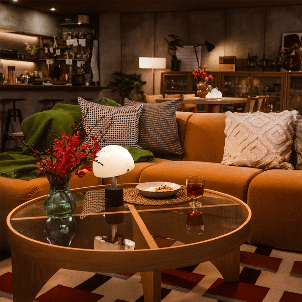 落ち着いたリビングで、キャメル色のソファとクッション、丸いガラステーブルとテーブルランプが、イケアのリビング＆ダイニングコーディネートを彩る。
