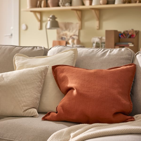 En pläd och tre kuddar, varav en med ett rödbrunt DYTÅG-kuddfodral, ligger på en ljusbeige EKTORP-soffa.