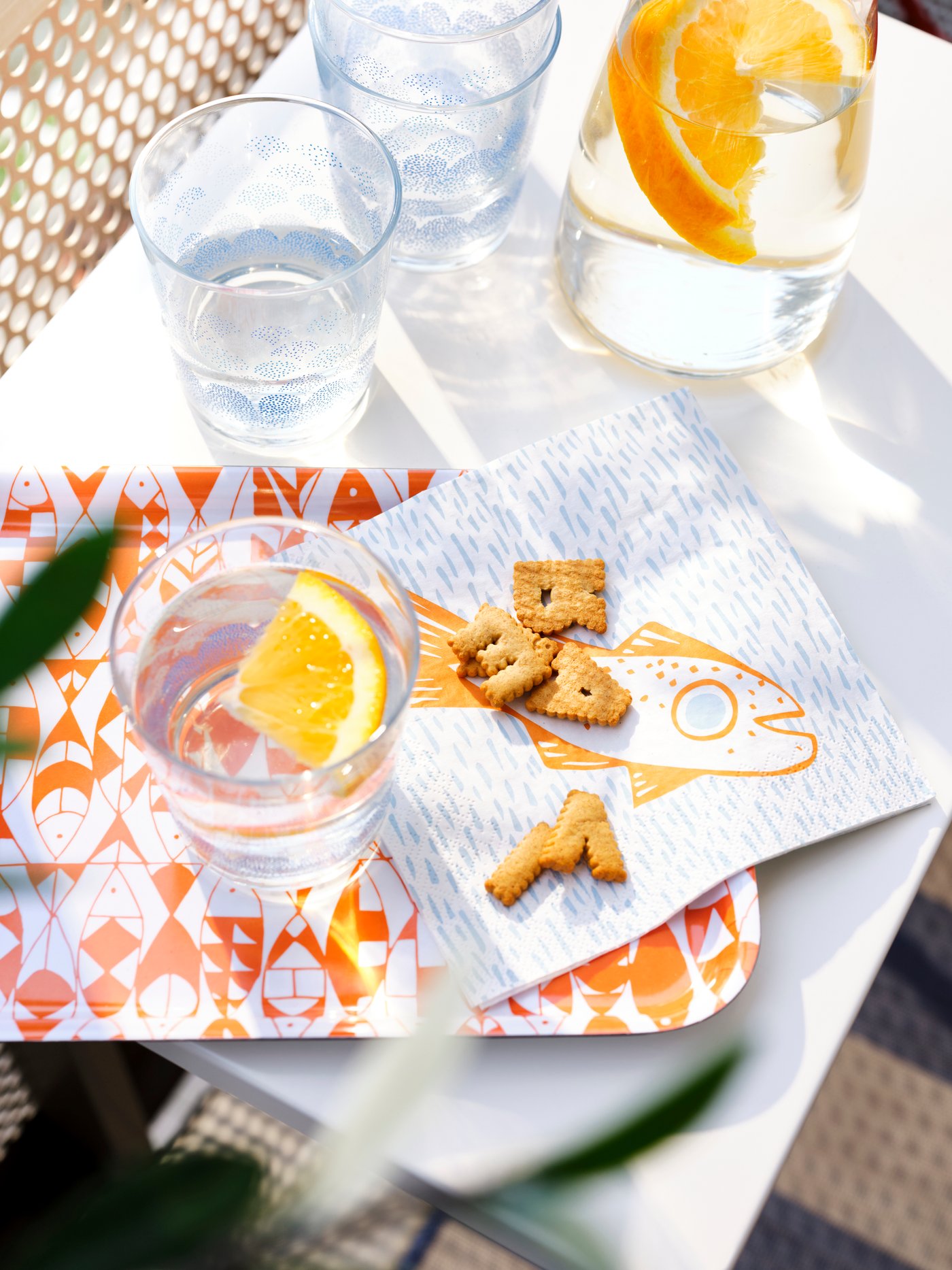 A tray with an orange/white pattern, painted glasses, a light blue/orange paper napkin, all from the SOMMARDRÖM collection.