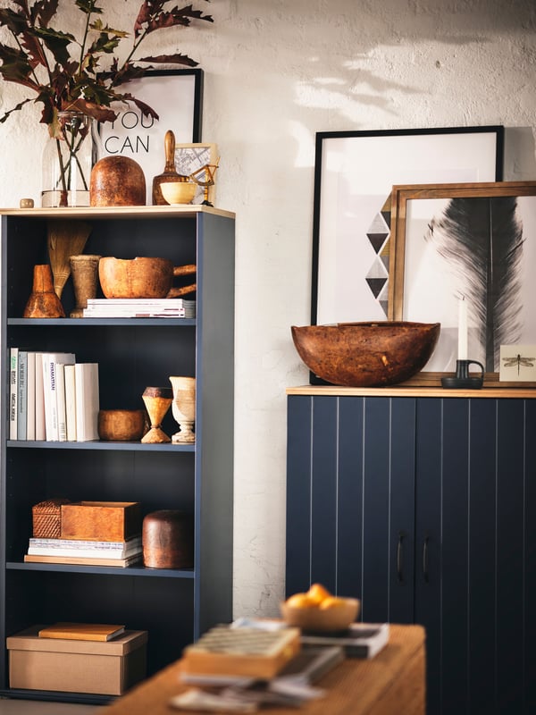 A light living room where a black-blue SKRUVBY bookcase and a SKRUVBY cabinet with doors stand slightly apart along a wall.