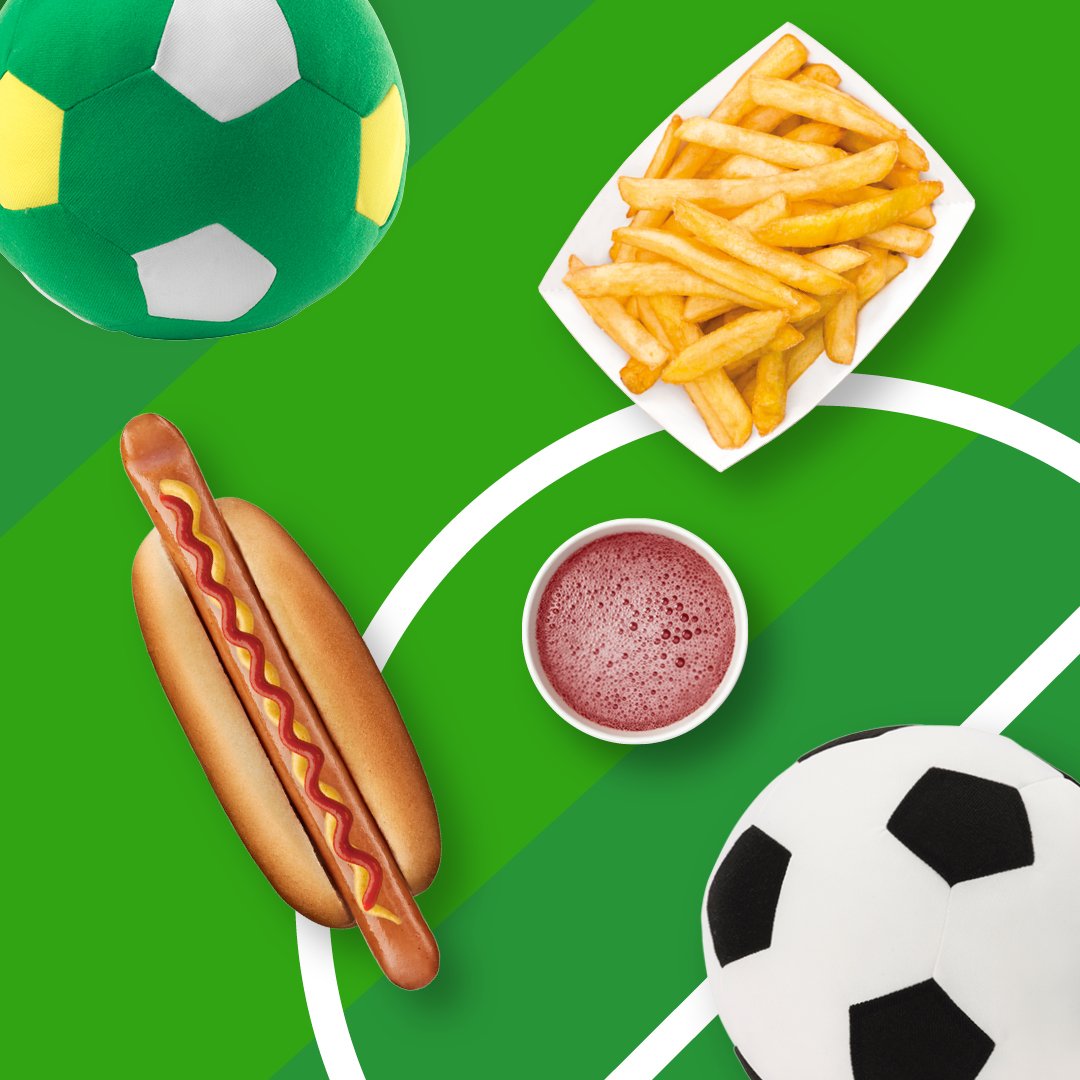 Na zielonym tle boiska widoczna piłka do gry nożnej, hot dog, frytki i napój w kubku papierowym