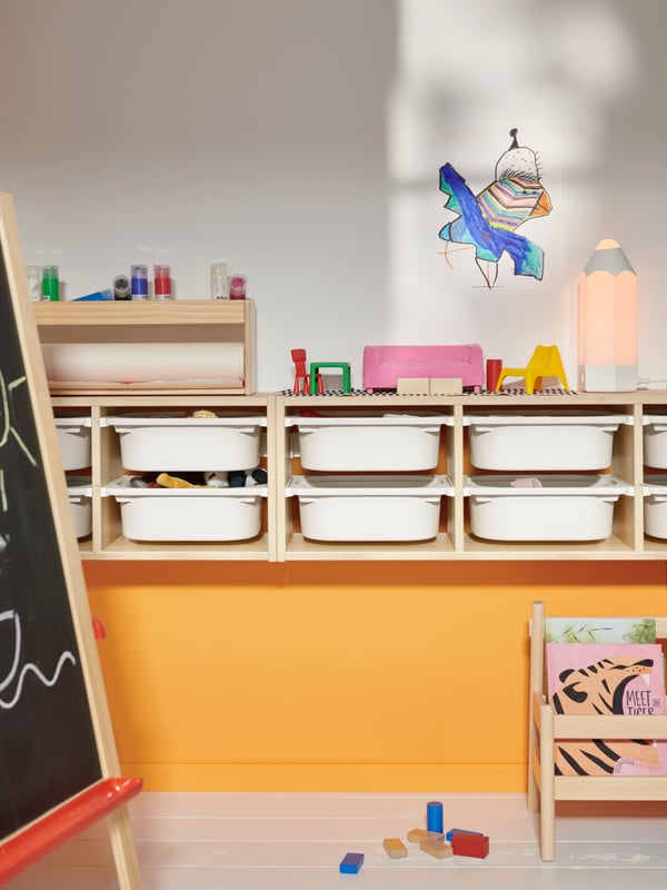 Two TROFAST wall storage units in light white stained pine on an orange and white wall, full of white TROFAST storage boxes.