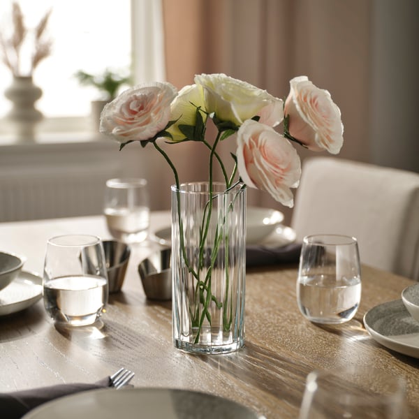 A clear PÄRLGLADA vase with GULDSPETT paper flowers on a set table.