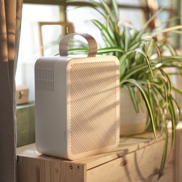 An UPPÅTVIND air purifier and a plant on top of a pine RAST chest with 3 drawers that’s in front of a window.