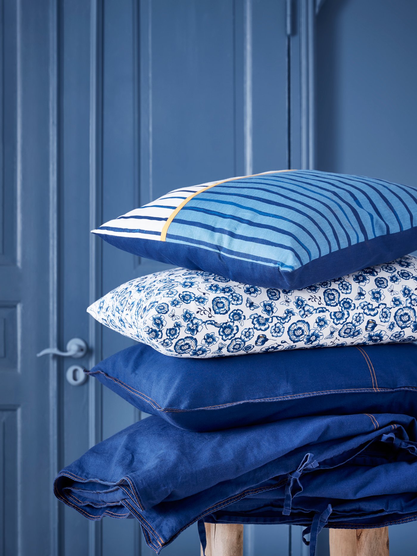 SÅNGLÄRKA bed linen and SÅNGLÄRKA cushions with different patterns are piled on top of each other in a blue room.