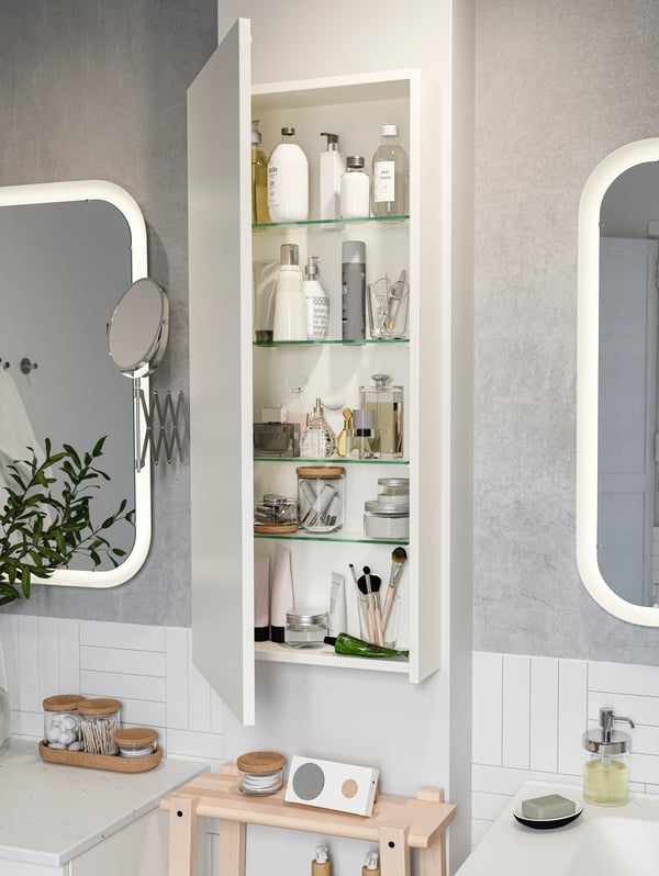 GODMORGON high cabinet is wall-mounted between two bathroom mirrors. The door is open, and products are on the shelves.