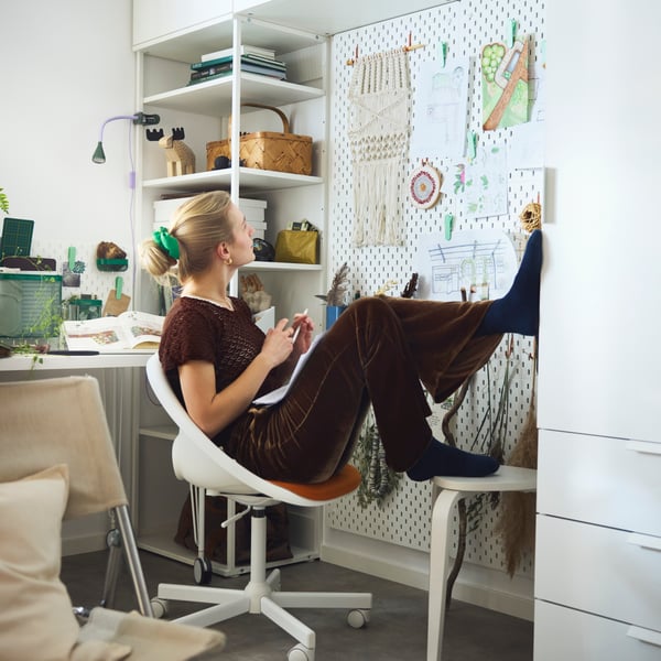 Eine Person sitzt an einem Schreibtisch und guckt gegen eine Wand mit SKÅDIS Lochplatten.