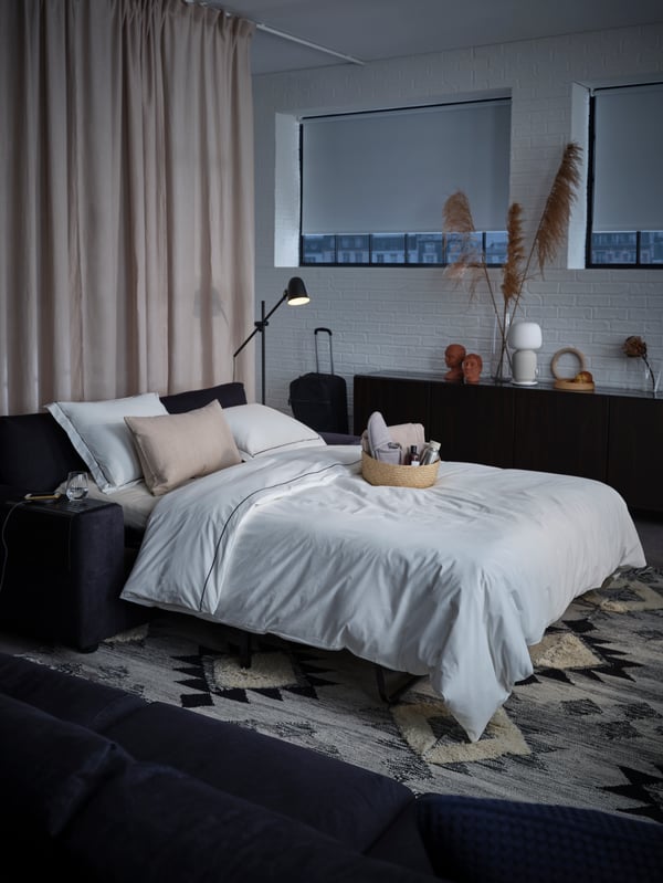 A 2-seat sofa-bed, beige block-out curtains, a quilt and pillows, a welcome basket with towels and toiletries.