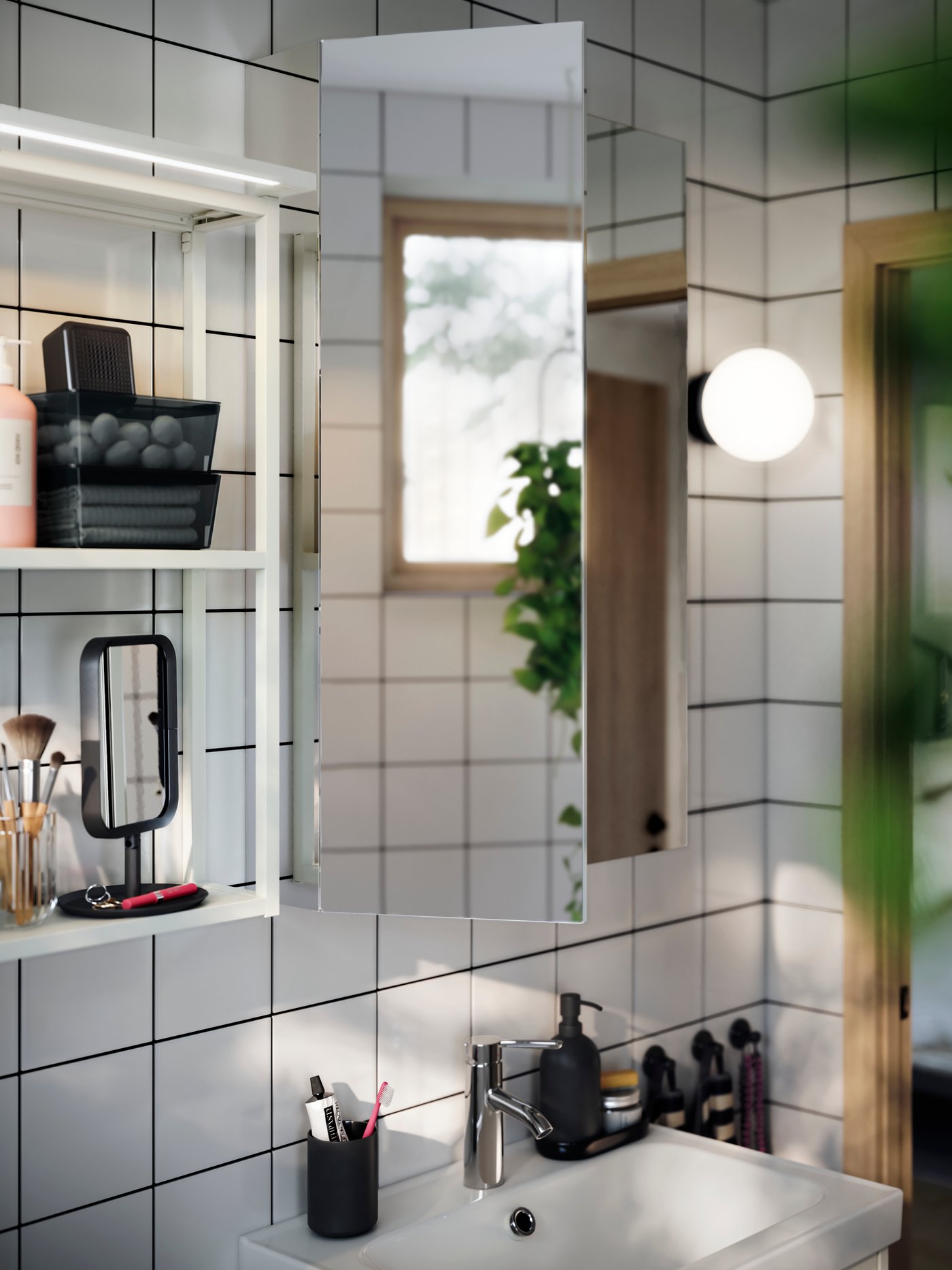 Un armario con espejo LETTAN poco profundo y minimalista sobre el lavabo de un cuarto de baño. Estantes de pared abiertos blancos colgando a su lado.