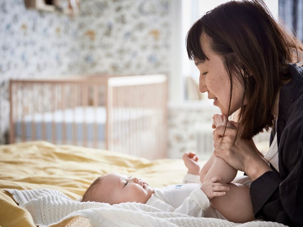 A mother holding a baby with a speckled romper in her lap, with a yellow/black KLAPPA rattle next to the baby.