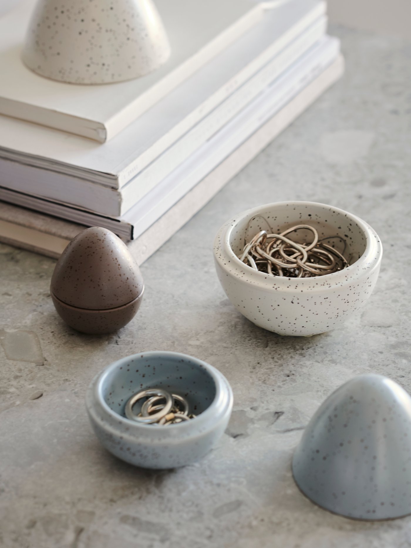 A set of three RÅDFRÅGA decorative eggs with books in the background. Two eggs are open to reveal jewellery stored within.