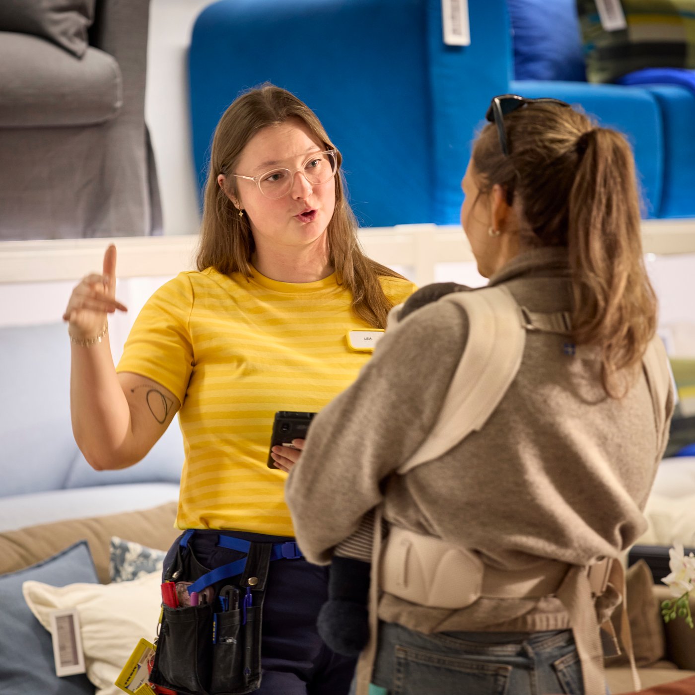 An IKEA employee in a store is talking to a customer in the Sofa department.