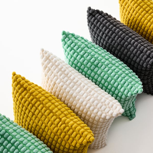 A row of cushions with SVARPOPPEL cushion covers in yellow, anthracite, light green and off-white.