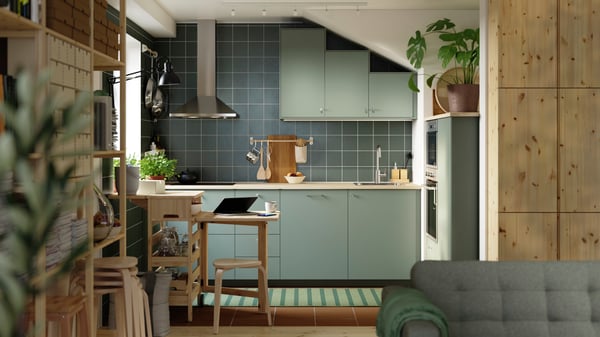 A green L-shaped kitchen has grey green NICKEBO fronts and a RESARÖ mobile drop-leaf table with storage and some stools.