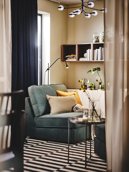Zonă de living cu o canapea extensibilă KIVIK cu perne și o măsuță așezată pe un covor STOCKHOLM 2017 cu design decupat.