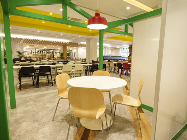 赤い照明と緑の柱がある室内で、円形テーブルを囲んで椅子が配置されている様子