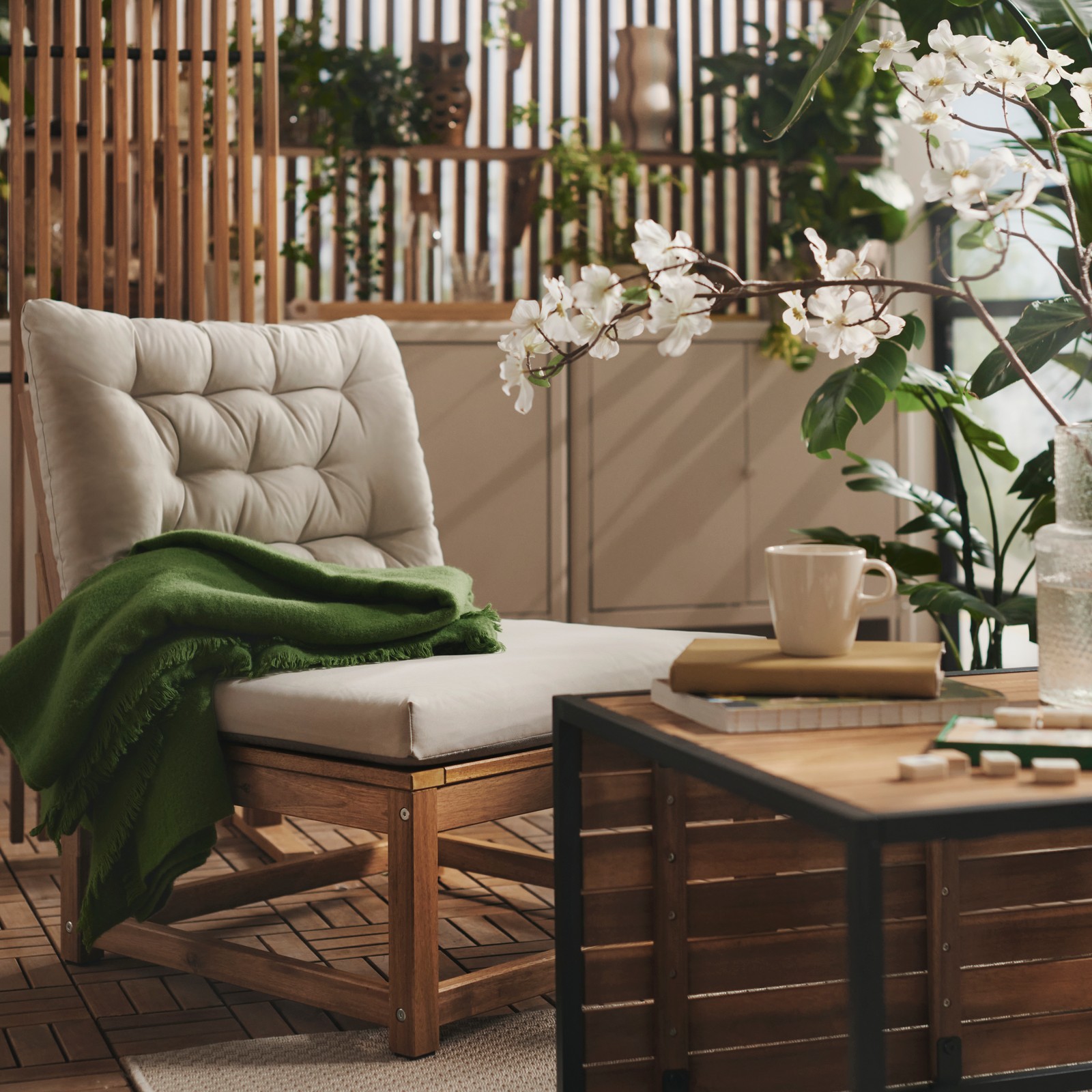 A balcony with greenery features a light brown stained NÄMMARÖ easy chair with light grey-beige cushions and a wooden table.