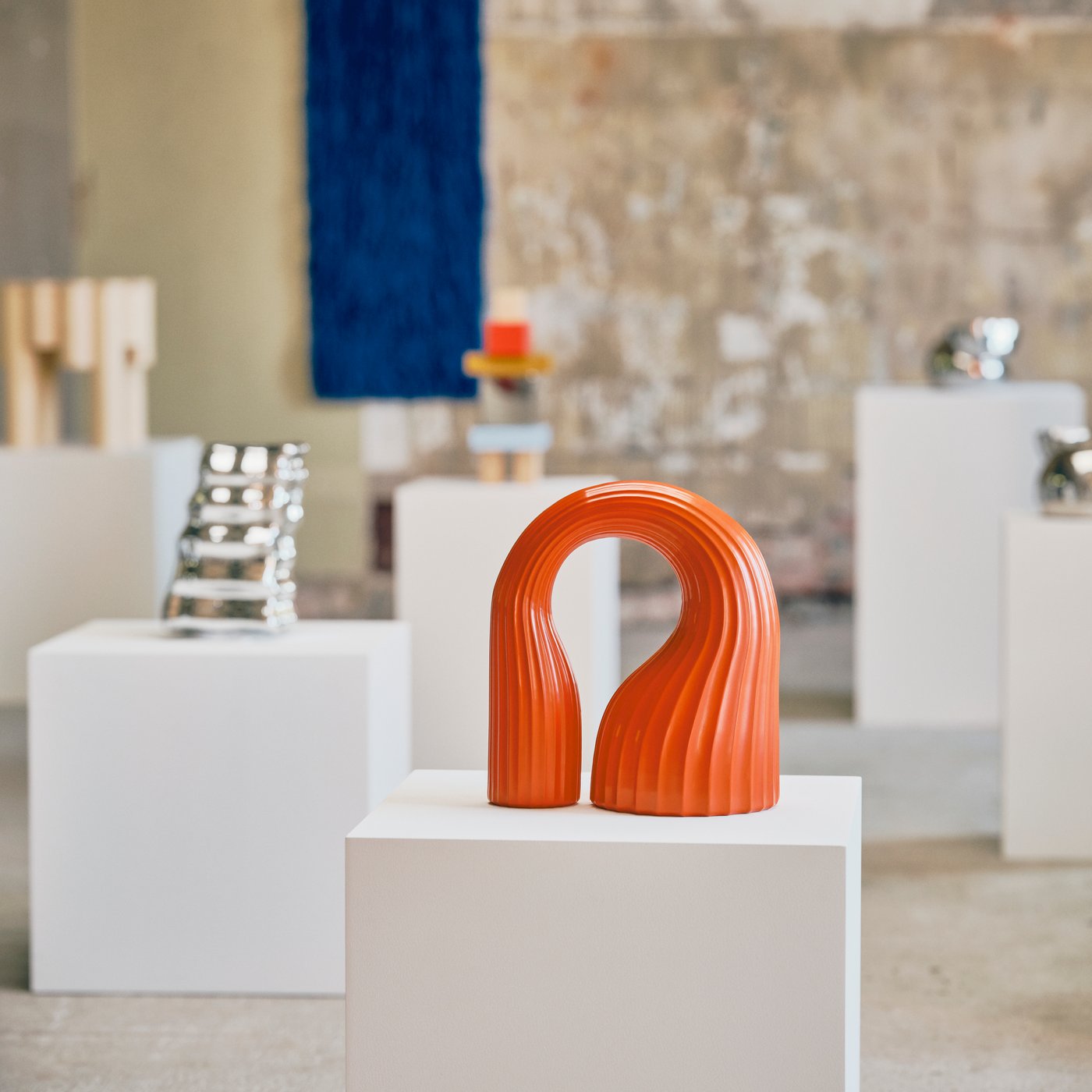 IKEA KONSTRUNDA art objects on white pedestals in a rough gallery style studio, with an orange sculpture nearest the camera.