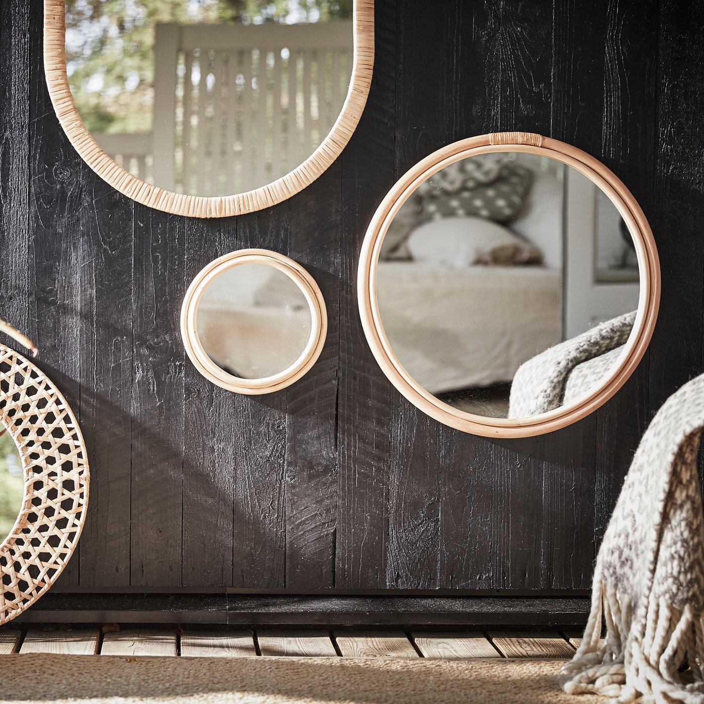 Varios espejos redondos de varios tamaños con marcos de ratán se cuelgan de una superficie de madera oscura para formar un punto focal.